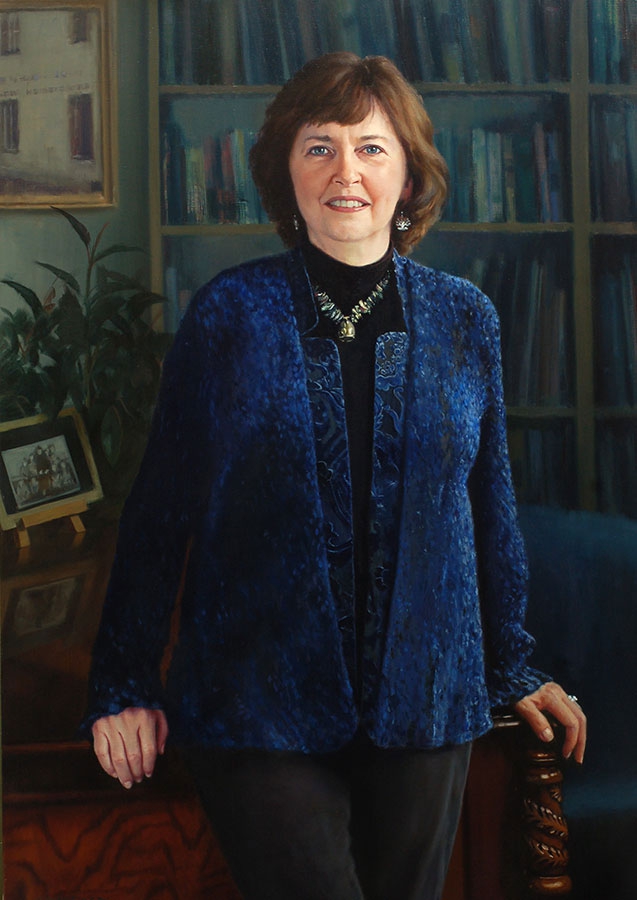 commissioned portrait of woman in blue standing in an academic office space.