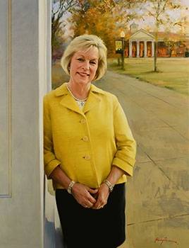 commissioned portrait of woman dressed in yellow and black, leaning on a building with campus in background.