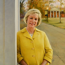 commissioned portrait of woman dressed in yellow and black, leaning on a building with campus in background.